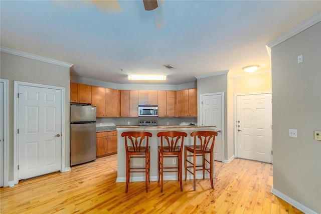 2502 Leon St Unit 305, Austin, TX 78705 - kitchen with appliances with stainless steel finishes, light wood-style flooring, a kitchen breakfast bar, brown cabinets, and ornamental molding