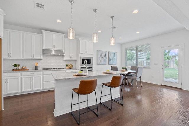 4409 Arques Ave, Round Rock, TX 78681 - kitchen featuring under cabinet range hood, cooktop, white cabinetry, tasteful backsplash, and dark wood finished floors