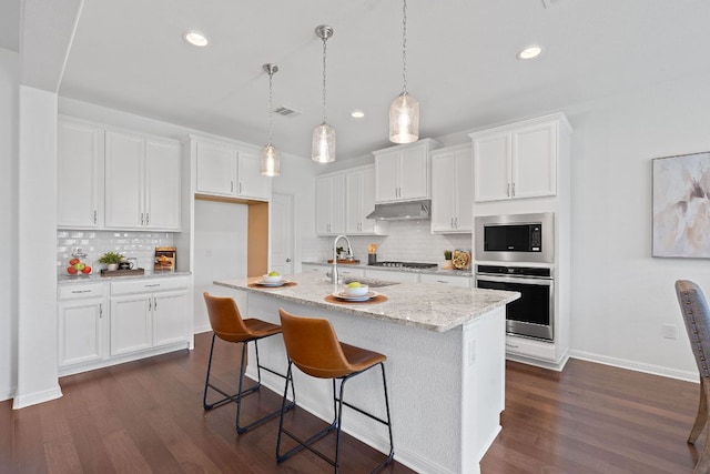 4409 Arques Ave, Round Rock, TX 78681 - kitchen with appliances with stainless steel finishes, under cabinet range hood, decorative backsplash, white cabinets, and dark wood-style flooring