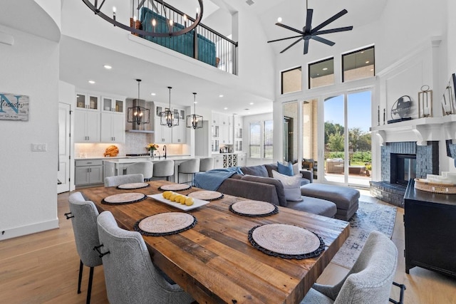 dining room with light wood-style flooring, ceiling fan, a glass covered fireplace, a towering ceiling, and a chandelier
