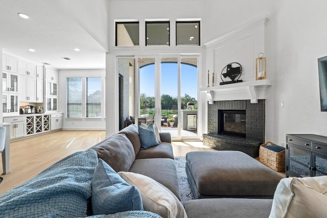 living room with a brick fireplace, light wood-style floors, recessed lighting, and a high ceiling