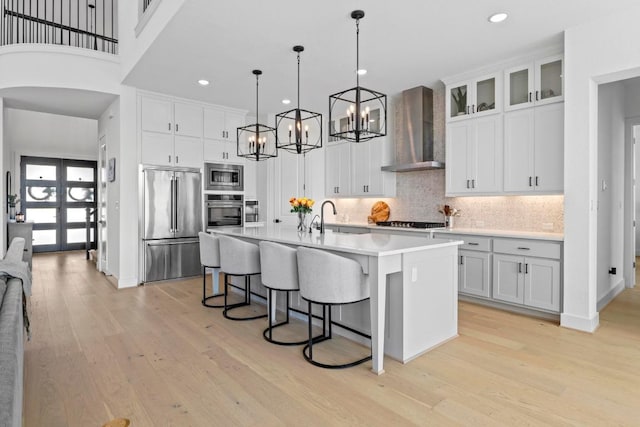kitchen with wall chimney range hood, appliances with stainless steel finishes, a chandelier, a breakfast bar, and light wood-style floors