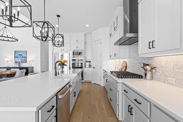 kitchen with a chandelier, wall chimney range hood, built in appliances, light wood-style floors, and recessed lighting