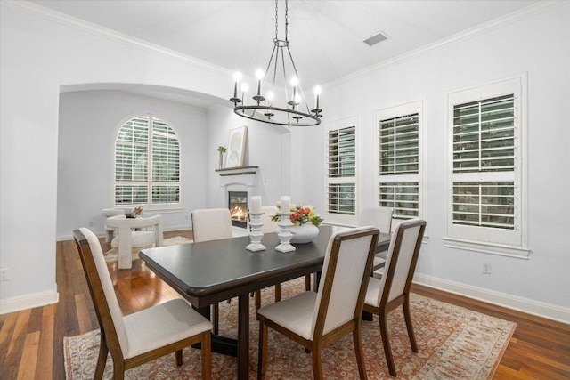 13212 Coleto Creek Trl, Austin, TX 78732 - dining area featuring a chandelier, wood finished floors, ornamental molding, a glass covered fireplace, and arched walkways