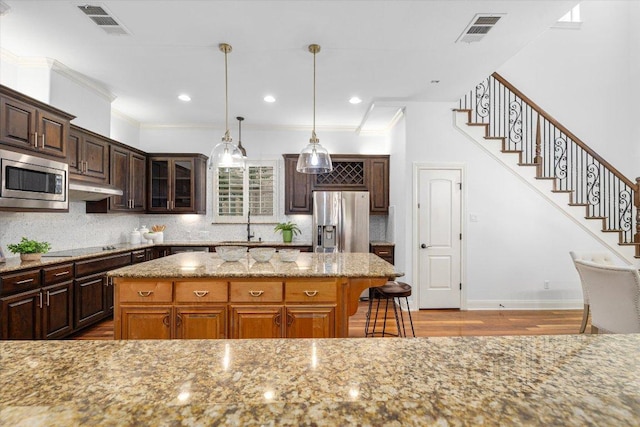 13212 Coleto Creek Trl, Austin, TX 78732 - kitchen featuring appliances with stainless steel finishes, under cabinet range hood, light stone counters, a center island, and wood finished floors