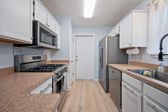 1009 Laurelleaf Dr, Pflugerville, TX 78660 - kitchen featuring stainless steel appliances, light wood-style flooring, white cabinets, and a textured ceiling