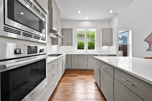 5904 Florencia Ln, Austin, TX 78724 - kitchen with gray cabinetry, stainless steel appliances, light wood-style flooring, backsplash, and recessed lighting
