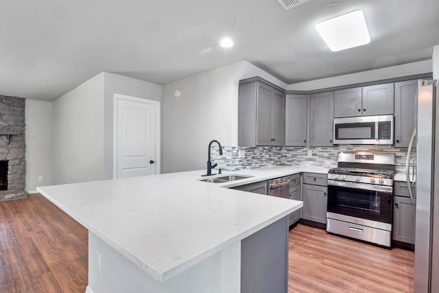 606 Elderberry Cv, Austin, TX 78745 - kitchen featuring appliances with stainless steel finishes, gray cabinets, a peninsula, backsplash, and light wood-style flooring
