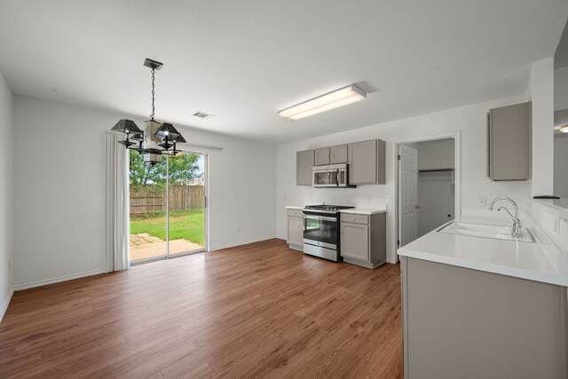 707 Eaglecreek Dr, Leander, TX 78641 - kitchen with gray cabinetry, stainless steel appliances, wood finished floors, a chandelier, and light countertops