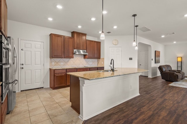 716 Madalin Rue Ct, Leander, TX 78641 - kitchen featuring under cabinet range hood, arched walkways, light stone counters, open floor plan, and tasteful backsplash