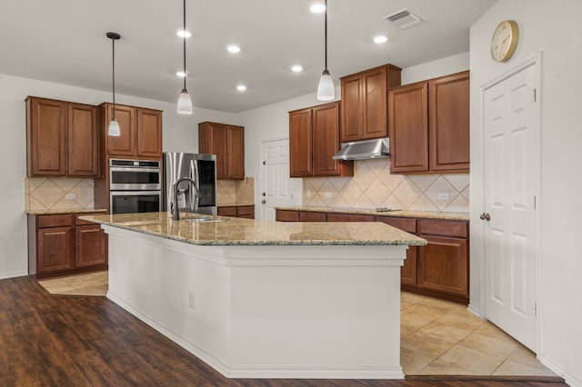 716 Madalin Rue Ct, Leander, TX 78641 - kitchen with under cabinet range hood, appliances with stainless steel finishes, a kitchen island with sink, tasteful backsplash, and recessed lighting
