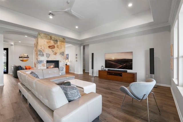 2105 Peoria Dr, Leander, TX 78641 - living room featuring arched walkways, ceiling fan, a tray ceiling, wood finished floors, and a tiled fireplace