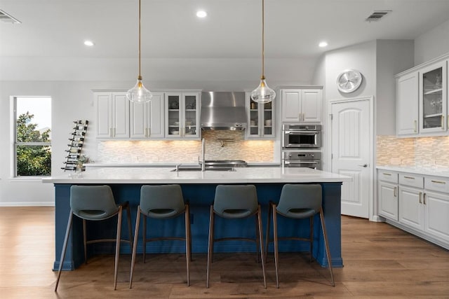 2105 Peoria Dr, Leander, TX 78641 - kitchen featuring wall chimney exhaust hood, a kitchen island with sink, white cabinets, light countertops, and recessed lighting