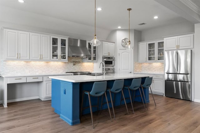2105 Peoria Dr, Leander, TX 78641 - kitchen featuring stainless steel fridge, wall chimney range hood, an island with sink, decorative backsplash, and light countertops