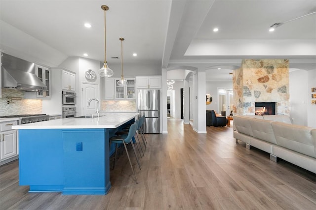 2105 Peoria Dr, Leander, TX 78641 - kitchen with wall chimney range hood, stainless steel appliances, open floor plan, a breakfast bar, and glass insert cabinets