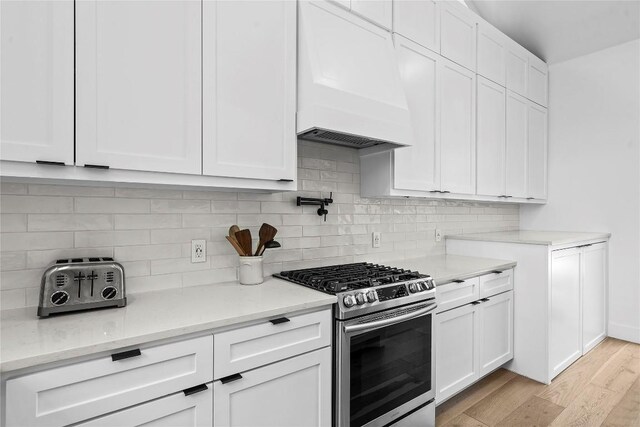 2216 Lindell Ave Unit 2, Austin, TX 78704 - kitchen with gas range, custom range hood, light wood finished floors, backsplash, and white cabinetry
