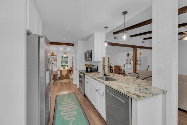 409 White Wing Way, Round Rock, TX 78664 - kitchen with stainless steel appliances, wood finished floors, white cabinets, light stone countertops, and beam ceiling