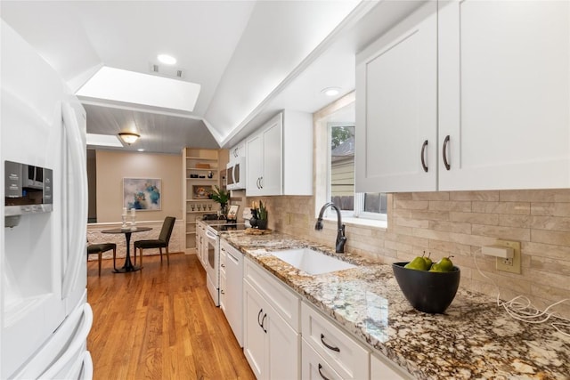 2206 Newfield Ln, Austin, TX 78703 - kitchen with white appliances, a skylight, white cabinetry, light wood-style flooring, and vaulted ceiling