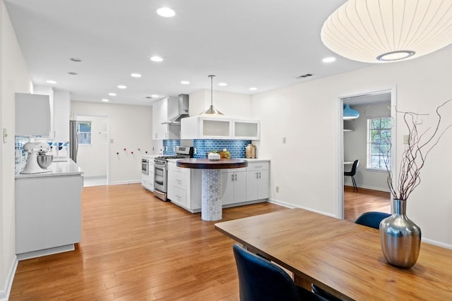 7710 Shoal Creek Blvd, Austin, TX 78757 - kitchen featuring appliances with stainless steel finishes, wall chimney exhaust hood, white cabinetry, decorative backsplash, and light wood-type flooring