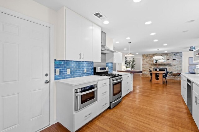 7710 Shoal Creek Blvd, Austin, TX 78757 - kitchen with stainless steel appliances, wall chimney range hood, light countertops, white cabinets, and light wood-style flooring