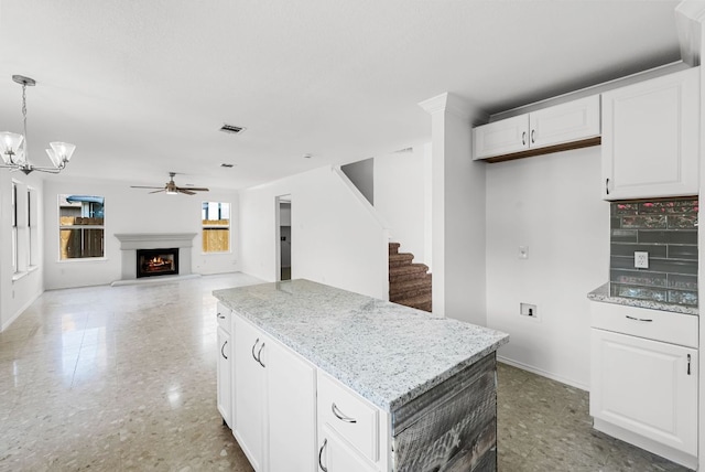 1213 Pathfinder Way, Round Rock, TX 78665 - kitchen with ceiling fan, a kitchen island, a warm lit fireplace, white cabinetry, and a chandelier