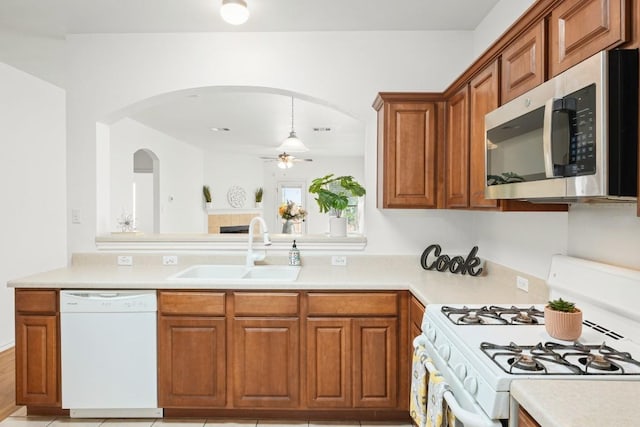 141 Ashwood N, Kyle, TX 78640 - kitchen featuring white appliances, arched walkways, brown cabinetry, and light countertops