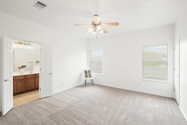 141 Ashwood N, Kyle, TX 78640 - unfurnished bedroom with light colored carpet, multiple windows, ensuite bathroom, and light tile patterned floors
