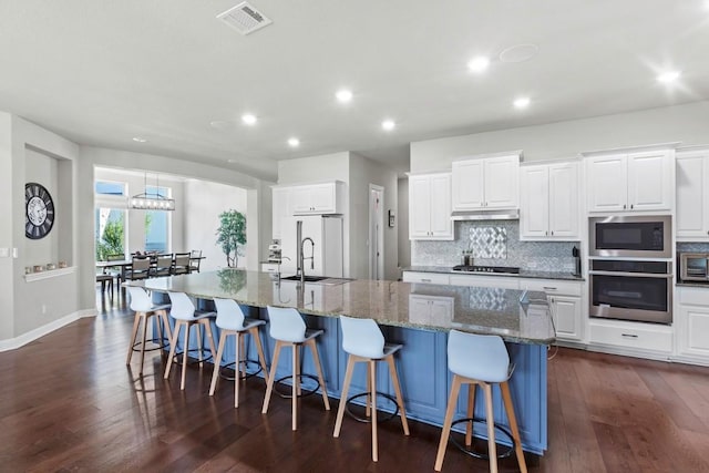 1720 Boscello Ct, Leander, TX 78641 - kitchen with stainless steel appliances, tasteful backsplash, a large island with sink, white cabinetry, and recessed lighting