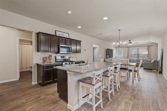3402 Tilmon Ln, Austin, TX 78725 - kitchen featuring stainless steel appliances, dark brown cabinets, open floor plan, light wood-style flooring, and a kitchen breakfast bar