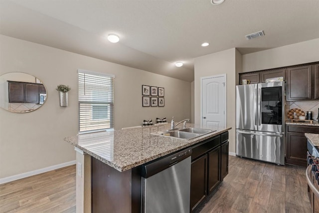 3402 Tilmon Ln, Austin, TX 78725 - kitchen featuring stainless steel appliances, wood finished floors, dark brown cabinets, a center island with sink, and recessed lighting
