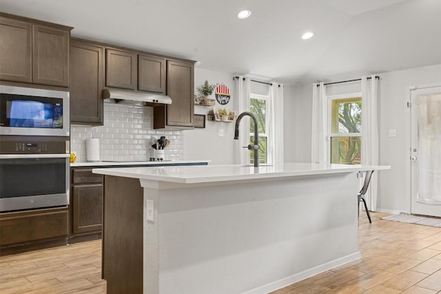 1703 Omaha Dr, Lago Vista, TX 78645 - kitchen featuring stainless steel appliances, under cabinet range hood, light countertops, tasteful backsplash, and a center island with sink