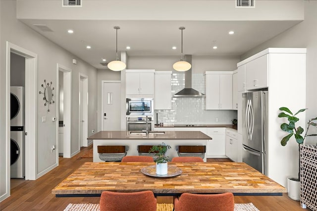 5921 Hiline Rd Unit 2404, Austin, TX 78734 - kitchen featuring wall chimney range hood, appliances with stainless steel finishes, stacked washer / dryer, a center island with sink, and dark wood-style flooring