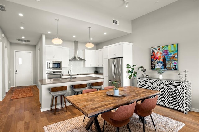 5921 Hiline Rd Unit 2404, Austin, TX 78734 - kitchen featuring wall chimney exhaust hood, appliances with stainless steel finishes, a kitchen island with sink, wood finished floors, and recessed lighting