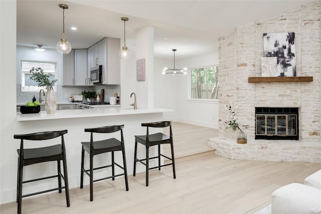 12044 Lincolnshire Dr, Austin, TX 78758 - kitchen featuring stainless steel microwave, gray cabinetry, light wood-type flooring, a breakfast bar area, and backsplash