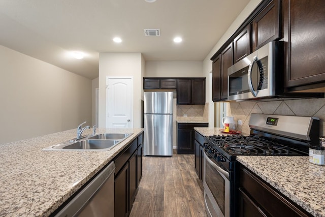 3305 Tilmon Ln, Austin, TX 78725 - kitchen with appliances with stainless steel finishes, wood finished floors, dark brown cabinetry, tasteful backsplash, and light stone counters
