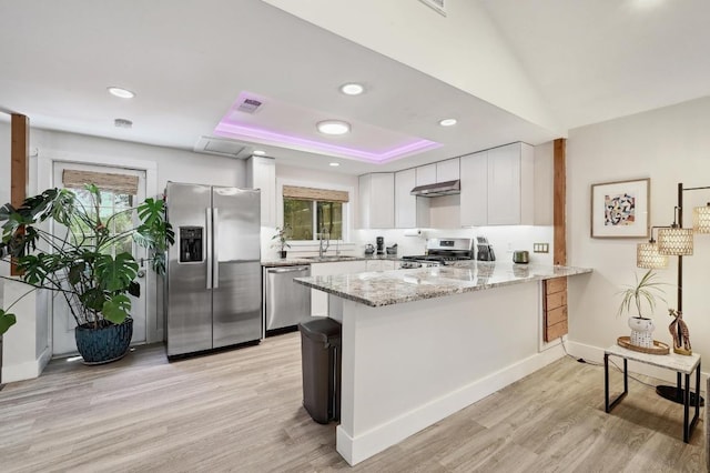 15507 Enid Dr, Austin, TX 78734 - kitchen with stainless steel appliances, a peninsula, light wood-type flooring, light stone counters, and white cabinetry