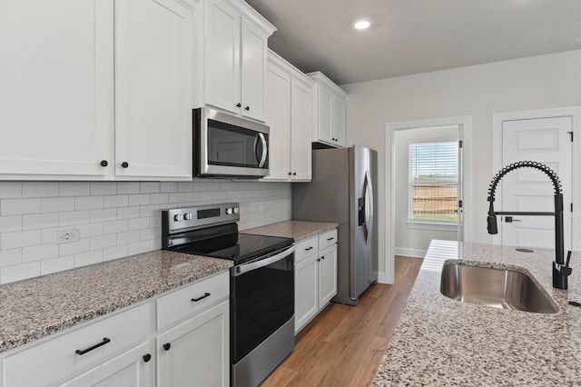9509 Demure Dr Unit 4, Manor, TX 78653 - kitchen with appliances with stainless steel finishes, white cabinetry, light wood-style floors, decorative backsplash, and recessed lighting