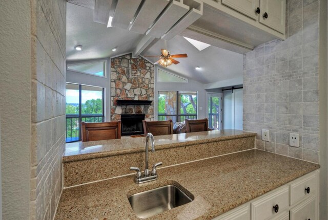 13111 Mansfield Dr, Austin, TX 78732 - kitchen featuring light stone countertops, a stone fireplace, white cabinetry, a ceiling fan, and backsplash