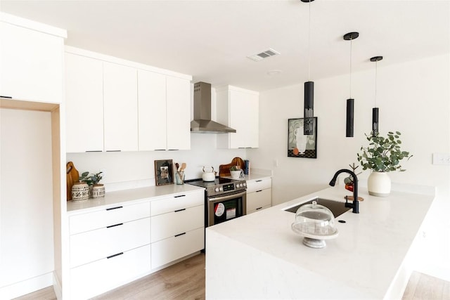 5731 Wellington Dr, Austin, TX 78723 - kitchen with wall chimney range hood, stainless steel range with electric stovetop, light wood finished floors, white cabinetry, and light countertops
