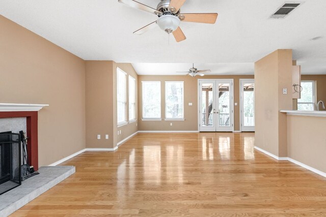 11978 Dorsett Rd, Austin, TX 78727 - unfurnished living room with light wood-type flooring, a ceiling fan, a tiled fireplace, and french doors