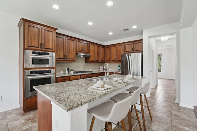 1508 Australis Cv, Austin, TX 78732 - kitchen featuring appliances with stainless steel finishes, a breakfast bar area, light stone counters, decorative backsplash, and recessed lighting