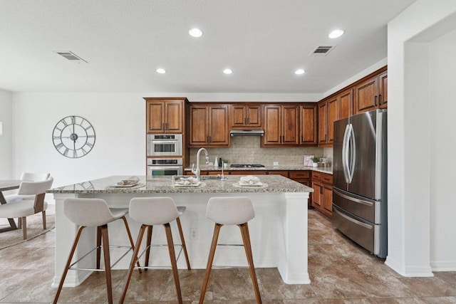 1508 Australis Cv, Austin, TX 78732 - kitchen with stainless steel appliances, under cabinet range hood, light stone countertops, a kitchen breakfast bar, and an island with sink