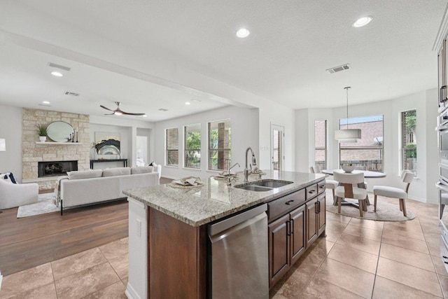1508 Australis Cv, Austin, TX 78732 - kitchen with stainless steel dishwasher, a stone fireplace, light stone counters, a center island with sink, and tile patterned floors
