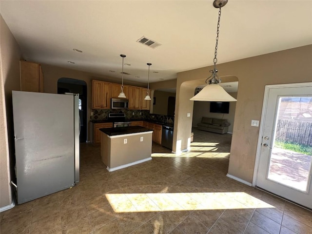 769 Apricot Dr, Kyle, TX 78640 - kitchen featuring arched walkways, stainless steel appliances, a kitchen island, dark countertops, and decorative backsplash