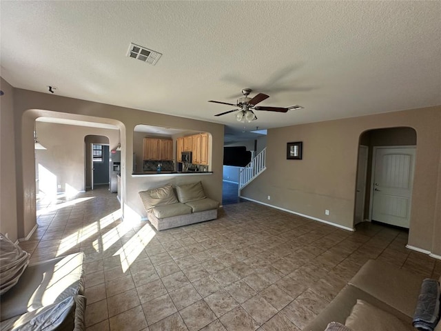 769 Apricot Dr, Kyle, TX 78640 - unfurnished living room featuring arched walkways, ceiling fan, a textured ceiling, stairs, and light tile patterned flooring