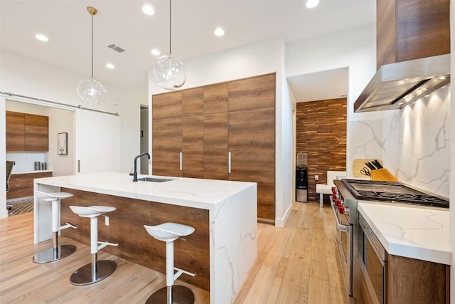 4103 Ridgelea Dr, Austin, TX 78731 - kitchen featuring wall chimney exhaust hood, high end stainless steel range oven, modern cabinets, light wood-style flooring, and brown cabinetry