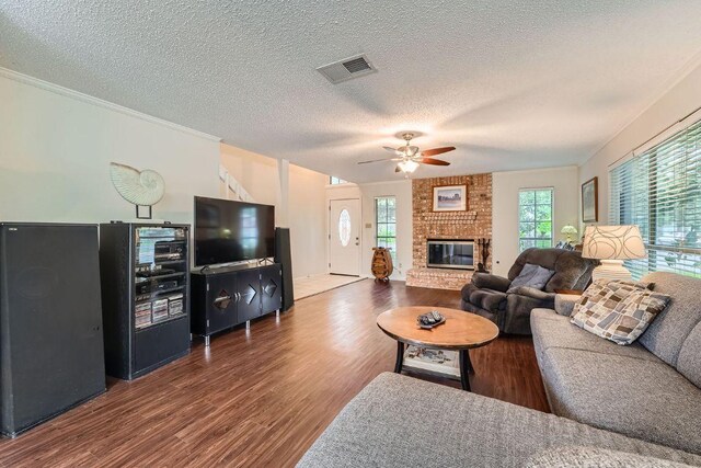 12711 Possum Hollow Dr, Austin, TX 78729 - living area with ceiling fan, dark wood-type flooring, a textured ceiling, a brick fireplace, and crown molding