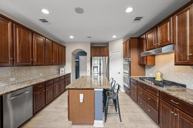 4605 Bat Falcon Dr, Austin, TX 78738 - kitchen featuring stainless steel appliances, under cabinet range hood, arched walkways, light stone countertops, and a breakfast bar
