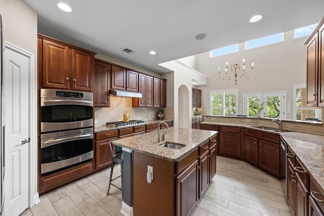 4605 Bat Falcon Dr, Austin, TX 78738 - kitchen with stainless steel appliances, arched walkways, under cabinet range hood, decorative backsplash, and light stone countertops