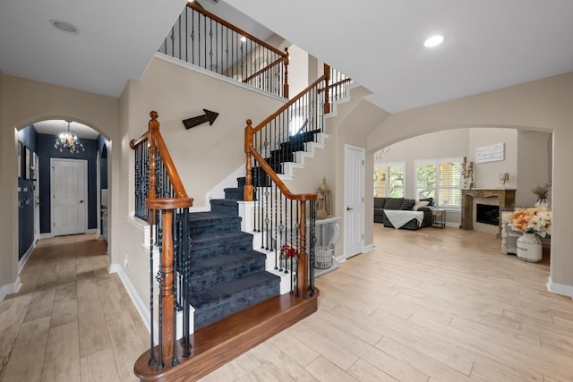 4605 Bat Falcon Dr, Austin, TX 78738 - stairs featuring arched walkways, wood finished floors, a chandelier, a fireplace, and a high ceiling
